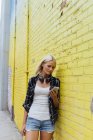 Junge Frau kontrolliert Handy an gelber Ziegelmauer — Stockfoto