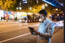 Businessman with digital tablet standing at a bus stop at night — Stock Photo