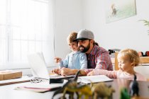 Father working at home, using laptop with his children on his lap — Stock Photo