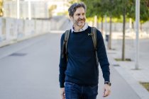 Homme mûr souriant avec un sac à dos dans la ville sur la route — Photo de stock