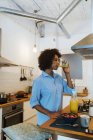 Mujer desayunando en su cocina, bebiendo jugo de naranja - foto de stock