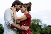 Pareja feliz en la naturaleza, de pie cara a cara, acariciándose mutuamente - foto de stock