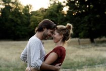 Pareja feliz en la naturaleza, de pie cara a cara, acariciándose mutuamente - foto de stock