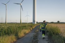 Technician walking on field path at a wind farm with climbing equipment — Stock Photo