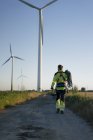 Technician walking on field path at a wind farm with climbing equipment — Stock Photo
