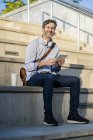 Porträt eines lächelnden reifen Mannes, der mit Tablet auf Stufen sitzt — Stockfoto