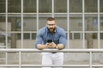 Портрет бородатого хіпстера бізнесмена з смартфоном спираючись на перила — стокове фото