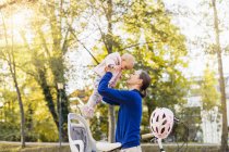 Mother and daughter riding bicycle, lifting baby from children seat — Stock Photo