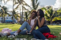 Two happy female friends relaxing in a park and listening to music — Stock Photo