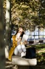 Женщина сидит на скамейке в парке с помощью планшета и пьет кофе — стоковое фото