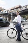 Alemania, Berlín, retrato de hombre de negocios con la bicicleta y la bolsa de ordenador portátil de pie en el pavimento - foto de stock