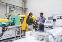 Empresario y mujer teniendo una reunión frente a robots industriales en una empresa de alta tecnología - foto de stock