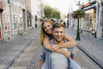 Netherlands, Maastricht, portrait of happy young couple in the city, man carrying woman on back, piggyback — Stock Photo