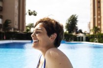 Rire jeune femme aux cheveux bruns courts relaxant à la piscine — Photo de stock