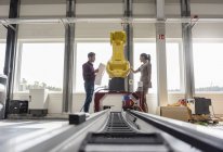 Бизнесмен и женщина встречаются перед промышленными роботами в высокотехнологичной компании — стоковое фото
