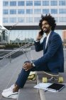 Espagne, Barcelone, jeune homme d'affaires assis à l'extérieur dans la ville et utilisant un téléphone portable et un ordinateur portable — Photo de stock