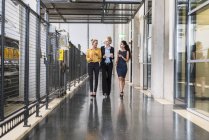 Tres mujeres con tableta caminando y hablando en el piso de la tienda de fábrica - foto de stock