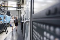 Две женщины с планшетом ходят и разговаривают в цехе завода — стоковое фото