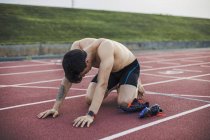 Athlète agenouillé sur une piste de tartan après avoir terminé une course — Photo de stock