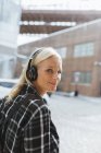 USA, New York City, Brooklyn, smiling young woman listening to music with headphones in the city — Stock Photo