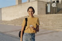 Portrait d'une jeune femme souriante tenant son téléphone portable à l'extérieur — Photo de stock