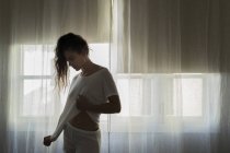 Молода жінка, що стоїть перед вікном в Білій білизні — стокове фото