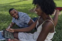 Happy young woman with boyfriend in a park using tablet — Stock Photo