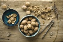 Whole and cracked walnuts in bowls on wood — Stock Photo