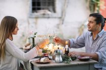 Coppia con un pasto romantico a lume di candela e bicchieri di vino clinking — Foto stock
