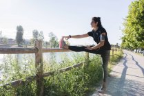 Sportive young woman stretching her leg at the riverside — Stock Photo
