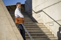 Зрелый мужчина с плечевой сумкой, стоящий на лестнице в городе — стоковое фото