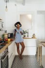 Женщина в наушниках, использует смартфон и пьет кофе на завтрак на кухне — стоковое фото