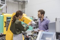 Empresario y mujer teniendo una reunión frente a robots industriales en una empresa de alta tecnología - foto de stock