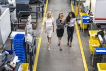 Três mulheres com tablet andando e conversando no chão da fábrica — Fotografia de Stock