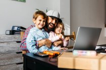 Батько працює вдома, ноутбук з дітьми на колінах. — стокове фото