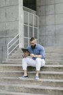 Бородатый хипстер-бизнесмен сидит на лестнице и использует цифровой планшет — стоковое фото