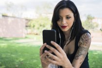 Portrait of smiling young woman with nose piercing and earphones taking selfie with smartphone — Stock Photo