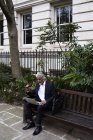 Senior businessman sitting on bench outdoors and working on laptop — Stock Photo