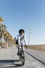Afro-américain faire du vélo sur une promenade de plage, écouter de la musique — Photo de stock