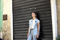 Retrato de mulher jovem na moda em pé na frente do obturador de rolo e olhando para a distância — Fotografia de Stock