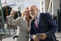 Senior businessman and businesswoman with baggage taking a selfie in the city — Stock Photo
