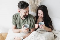 Feliz casal sentado na cama, beber café, se divertindo — Fotografia de Stock