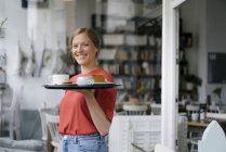 Portrait de jeune femme souriante servant du café et du gâteau dans un café — Photo de stock