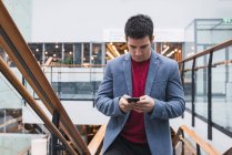 Businessman in lobby of a modern building, using smartphone — Stock Photo