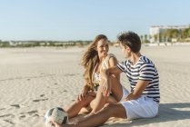 Lächelndes junges Paar sitzt mit Ball am Strand — Stockfoto