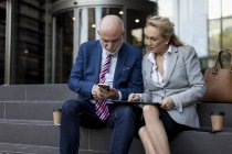 Uomo d'affari e donna d'affari anziani seduti sulle scale utilizzando il telefono cellulare e tablet — Foto stock