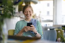 Laughing young woman looking on cell phone in a cafe — Stock Photo