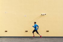 Sportive man running along yellow wall with CCTV camera — Stock Photo