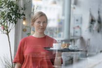 Portrait of young woman serving coffee and cake in a cafe — Stock Photo
