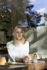 Portrait of blond woman in a cafe looking out of window — Stock Photo